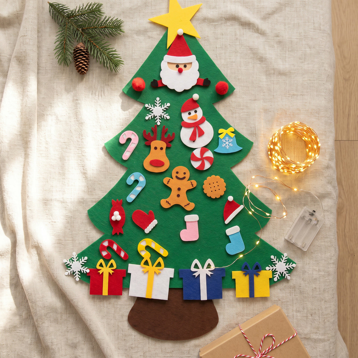 Felt Christmas tree laid flat on linen with fairy lights and a gift box
